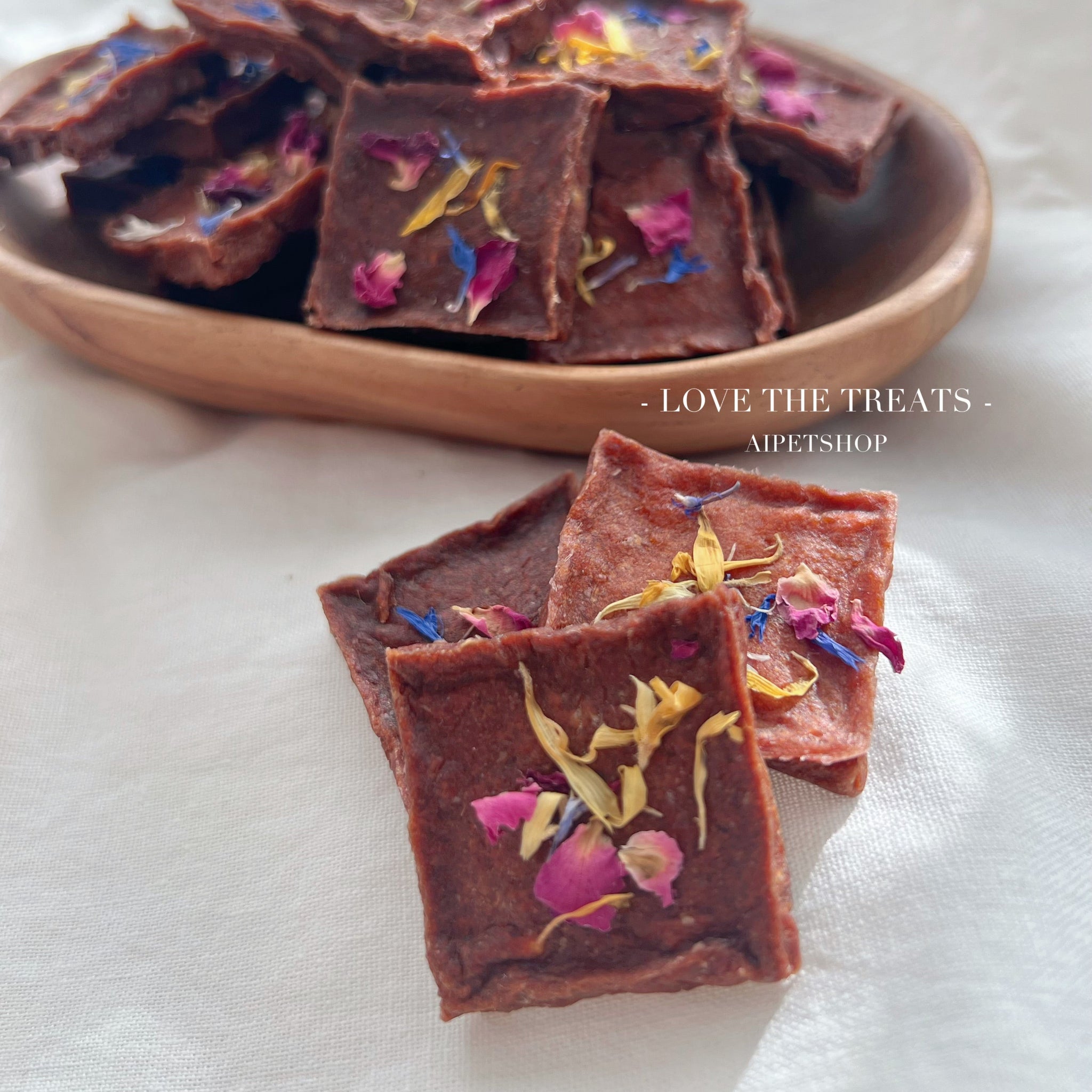 dog treats with dried flowers on a wooden plate and white surface, featuring the brand 'Aipetshop'.